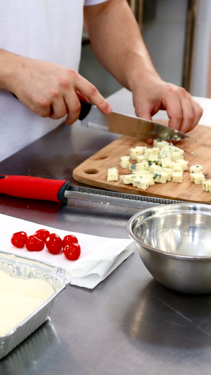 A chef chopping cheese on a cutting board in a professional kitchen with red utensils, ready for meal preparation.