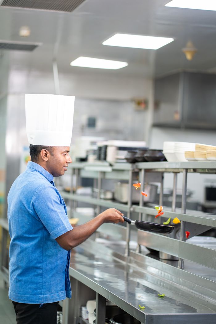 services-01 Chef skillfully cooking vegetables in a modern restaurant kitchen, emphasizing culinary expertise.