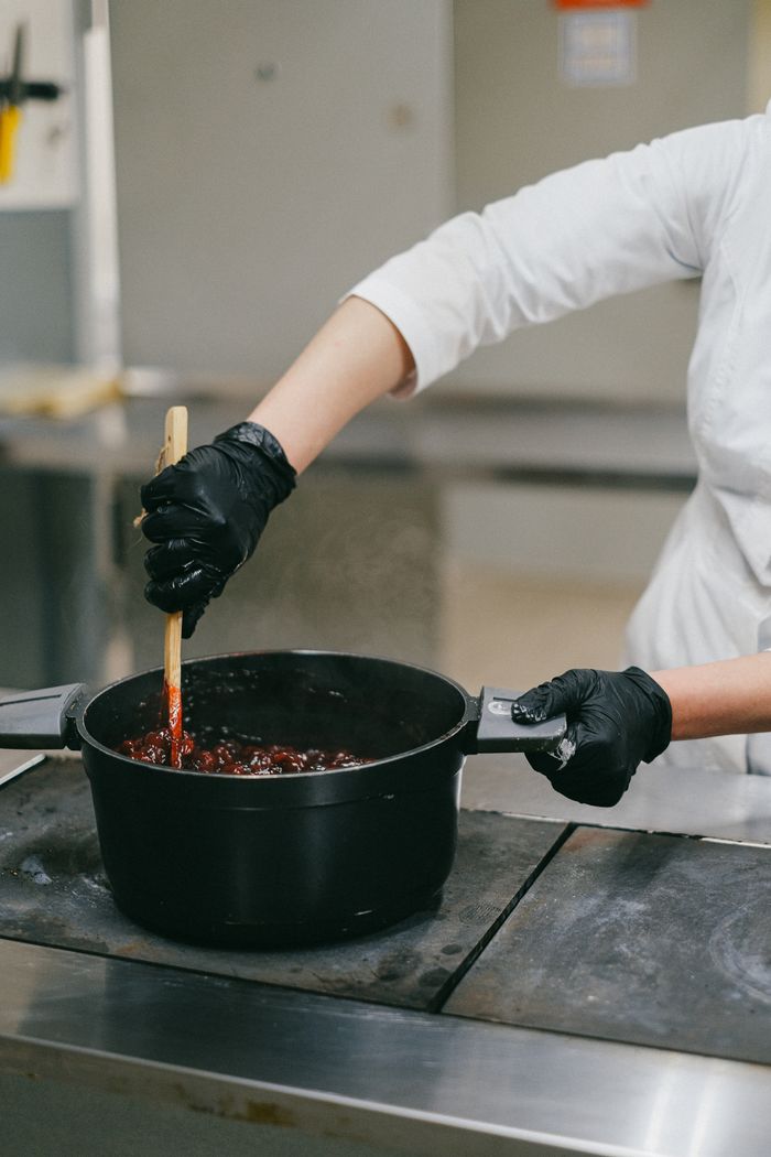 services-02 A chef stirs a dish in a black pot, highlighting culinary preparation in a professional kitchen.