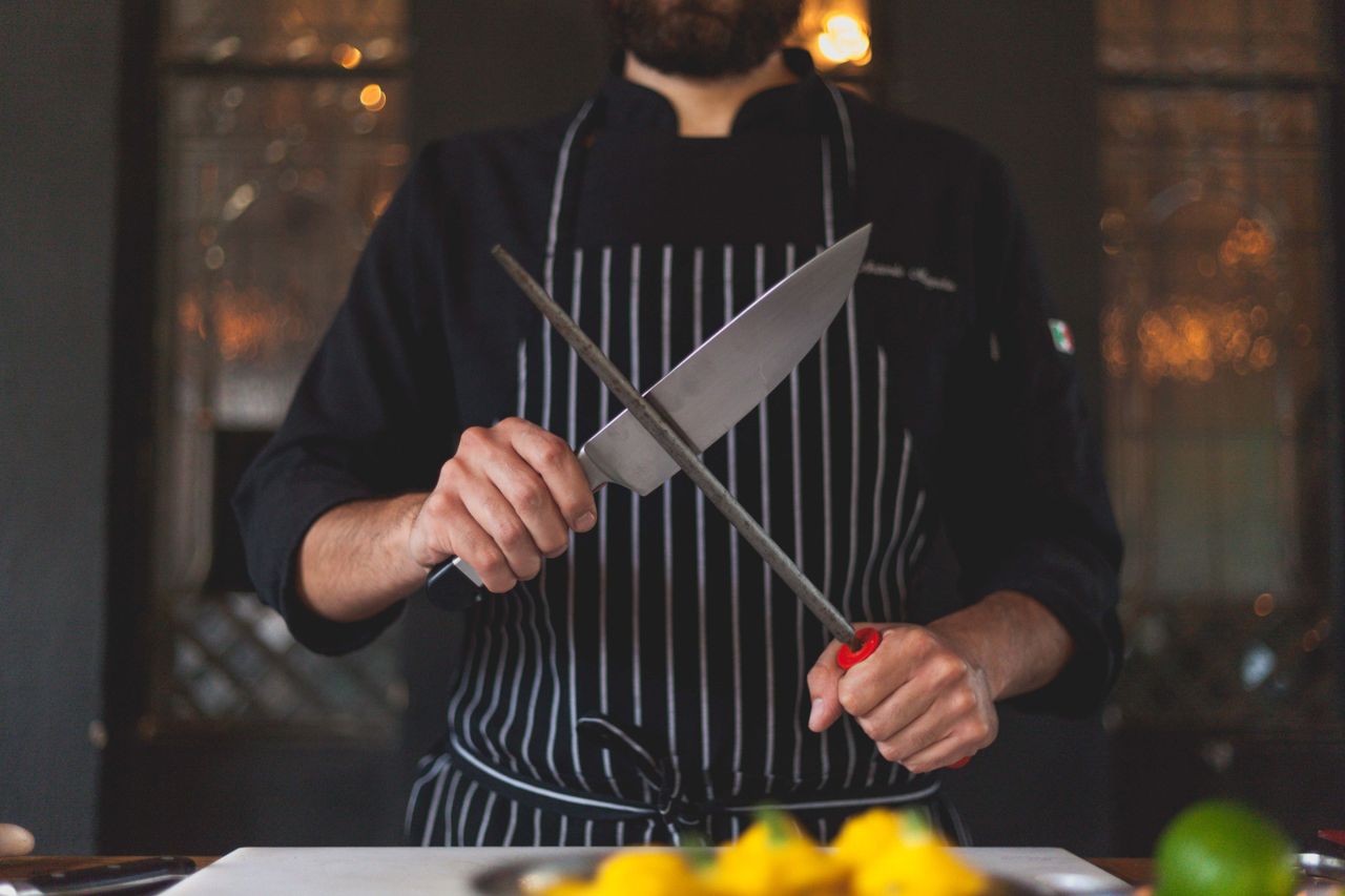 journey Chef sharpening a knife with a honing rod in a professional kitchen setting, focusing on precision and culinary skill.