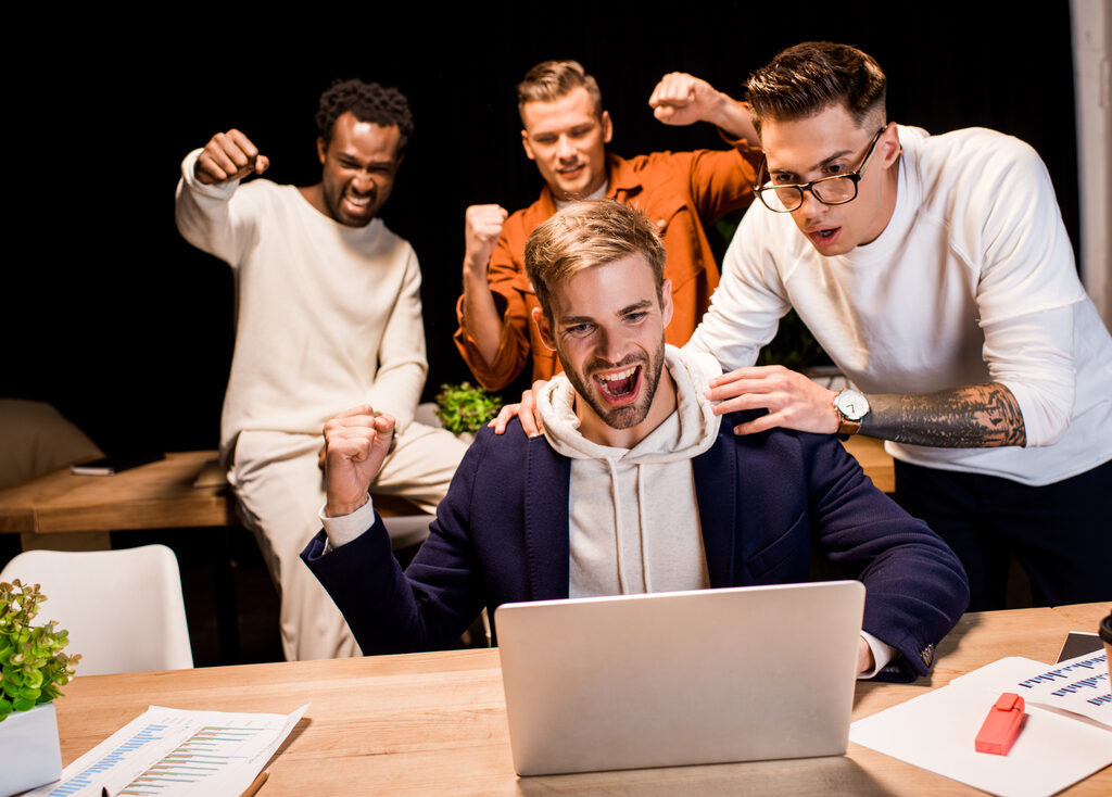 Essential LMS Features to Improve Online Learning Outcomes happy multicultural businesspeople showing winner gesture while working at night in office