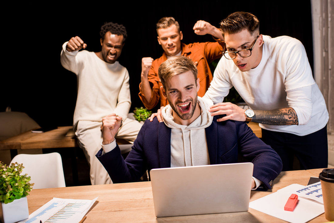 Essential LMS Features to Improve Online Learning Outcomes happy multicultural businesspeople showing winner gesture while working at night in office